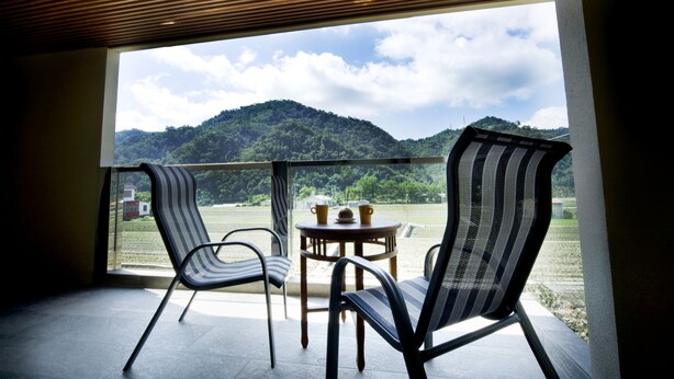 Ein Balkon mit zwei Stühlen und einem kleinen Tisch, der auf eine grüne Landschaft und Hügel blickt.