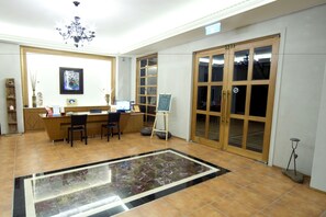 A spacious room with a reception desk, a chandelier, a large window, and a tiled floor. - Schokolake (Dahu)