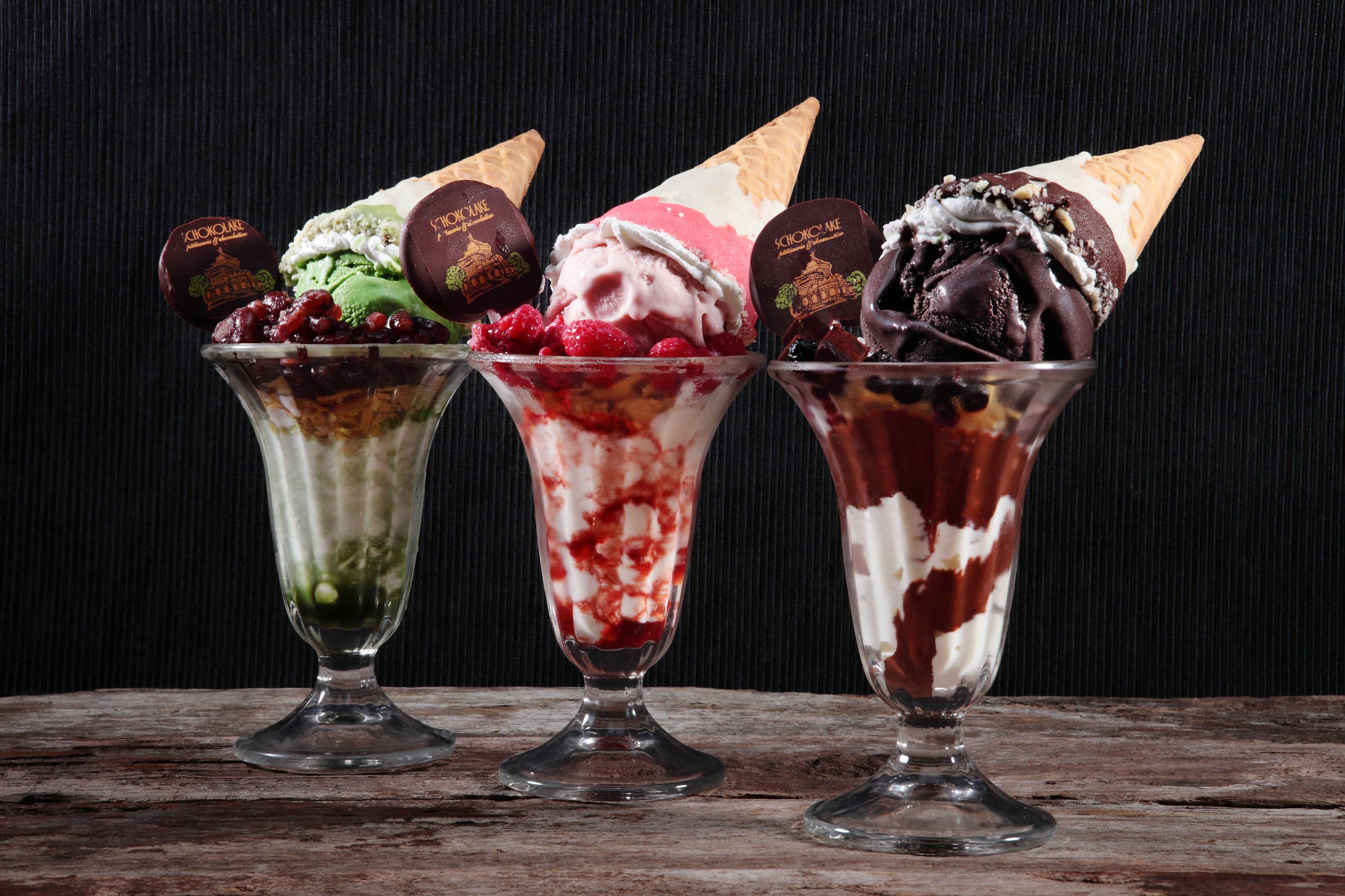 Drie ijsdesserts in glazen bekers op een houten ondergrond.