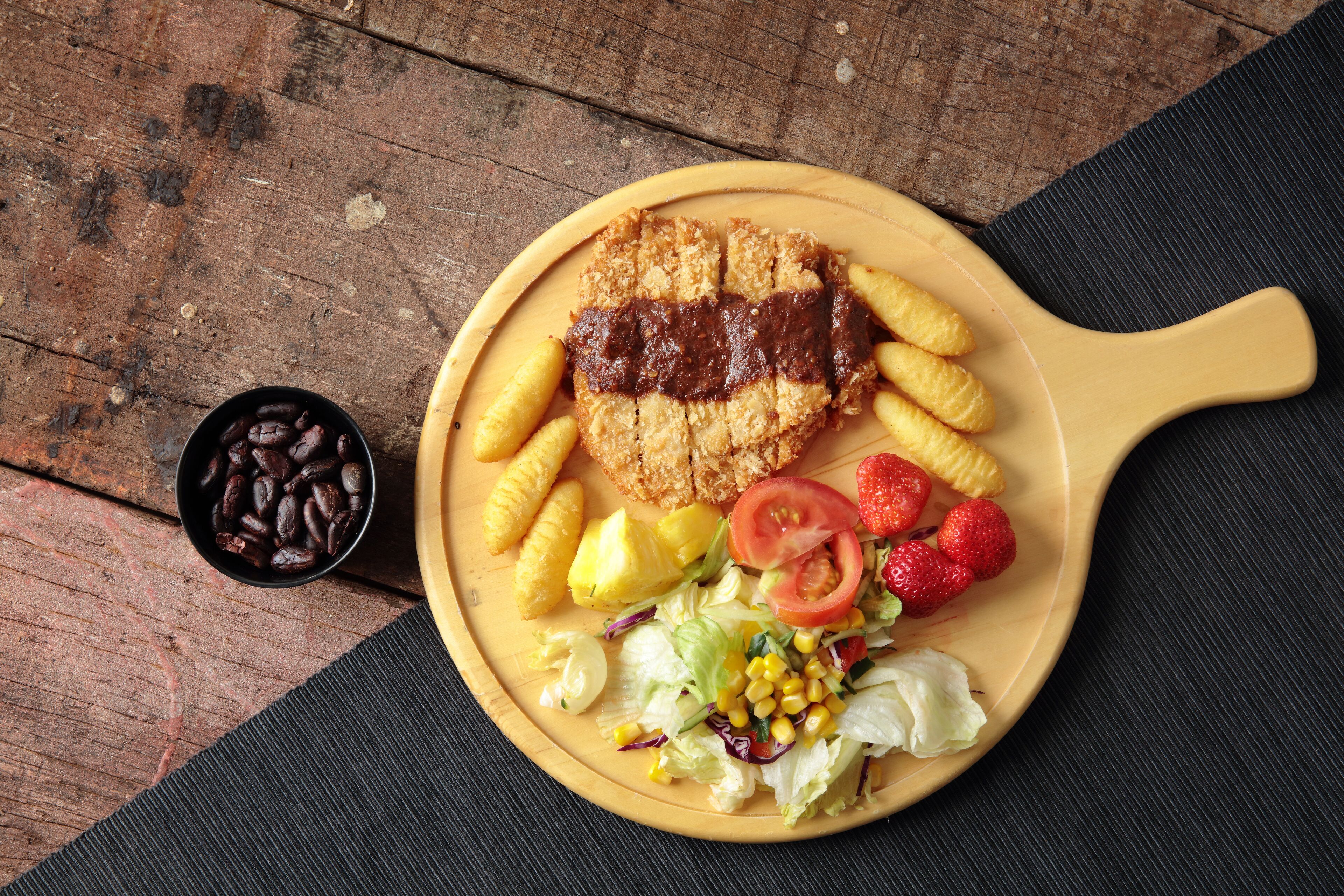 Une assiette contenant un steak grillé, du maïs, des fraises et une salade, le tout posé sur une table en bois.