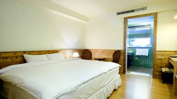 Una cama grande en una habitación con paredes y suelo de madera. Hay una silla y una mesita cerca de la cama.