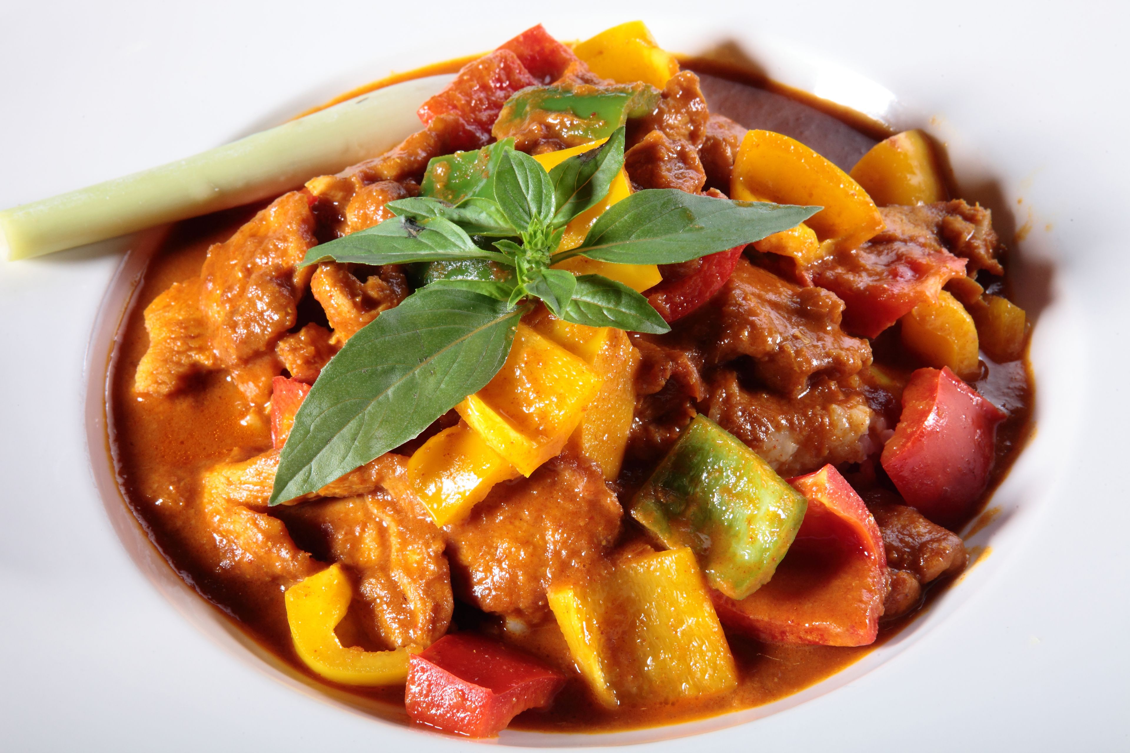 A bowl of stew with various vegetables and meat, garnished with a basil leaf.