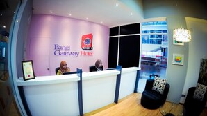 A reception area with a reception desk, two staff members, a large window, and a modern interior design. - Bangi Gateway Hotel (Bandar Baru Bangi)