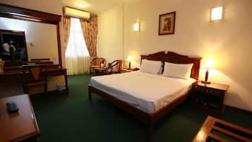 A hotel room with a bed, bedside tables, a desk, chairs, and a mirror.