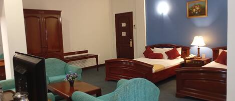 Quarto de hotel com uma cama, duas poltronas, uma mesa de centro, uma televisão e uma escrivaninha com cafeteira.