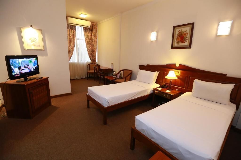 Ett hotellrum med två separata sängar, en tv på ett träskåp, ett skrivbord och en stol.