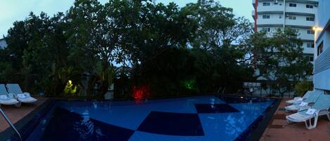 A swimming pool with lounge chairs and a building in the background.