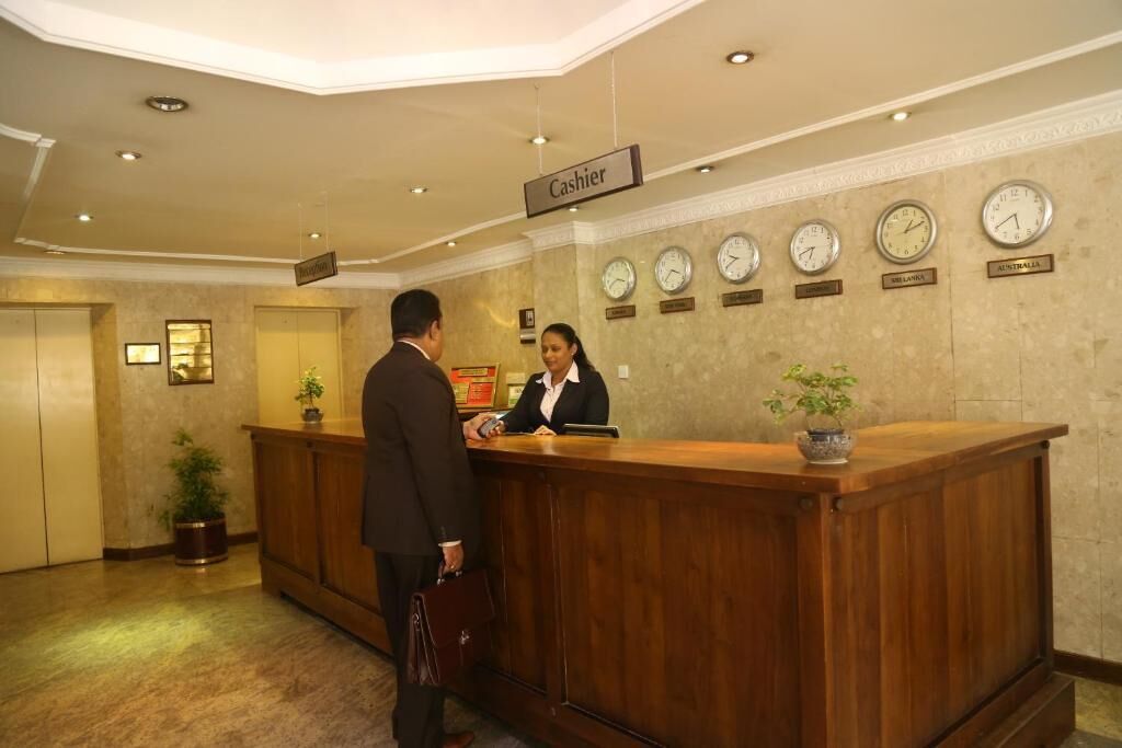 A hotel reception area with a wooden reception desk, a clock displaying the time, and a sign indicating the location of the cashier.