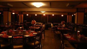 Un restaurante tenuemente iluminado con mesas y sillas redondas, un candelabro y una zona de bar.