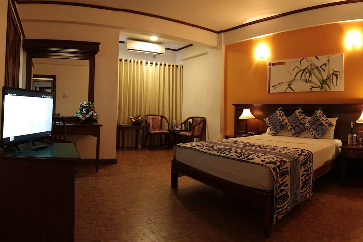 Una habitación de hotel con cama, lámparas de noche, un escritorio con computadora, una silla y un ventanal con cortinas.
