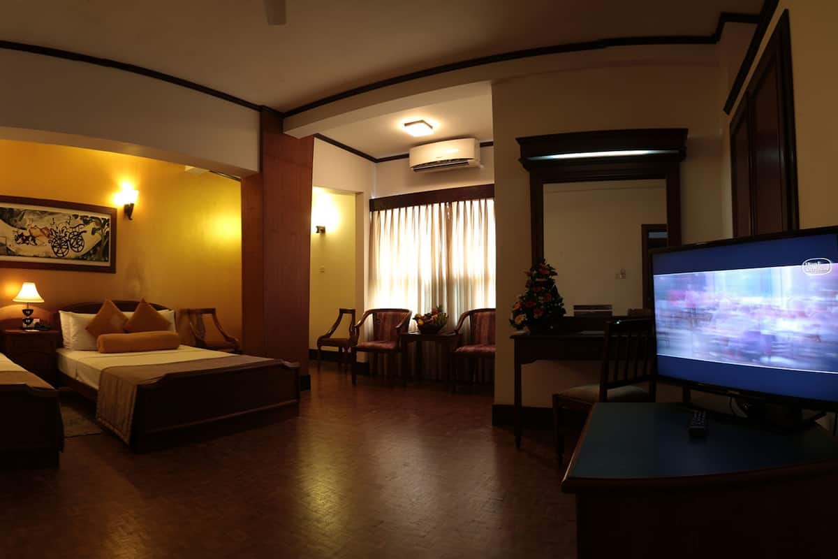 Habitación de hotel con dos camas, televisión, escritorio y zona de comedor.