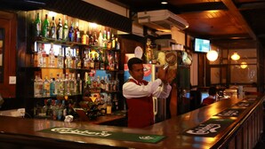 A bar with a variety of liquor bottles on shelves, a bartender, and a counter with a coaster. - Hotel Sapphire (Colombo)