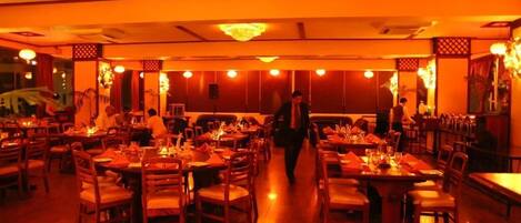 Un restaurante con varias mesas y sillas, suelo de madera y decoración tradicional.