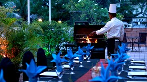 A chef grilling outdoors with tables set for dining, surrounded by greenery and a brick wall. - Hotel Sapphire (Colombo)