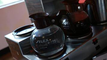 Eine Kaffeemaschine mit einem Glasbehälter und einem Metallkrug auf einer Edelstahl Arbeitsplatte.