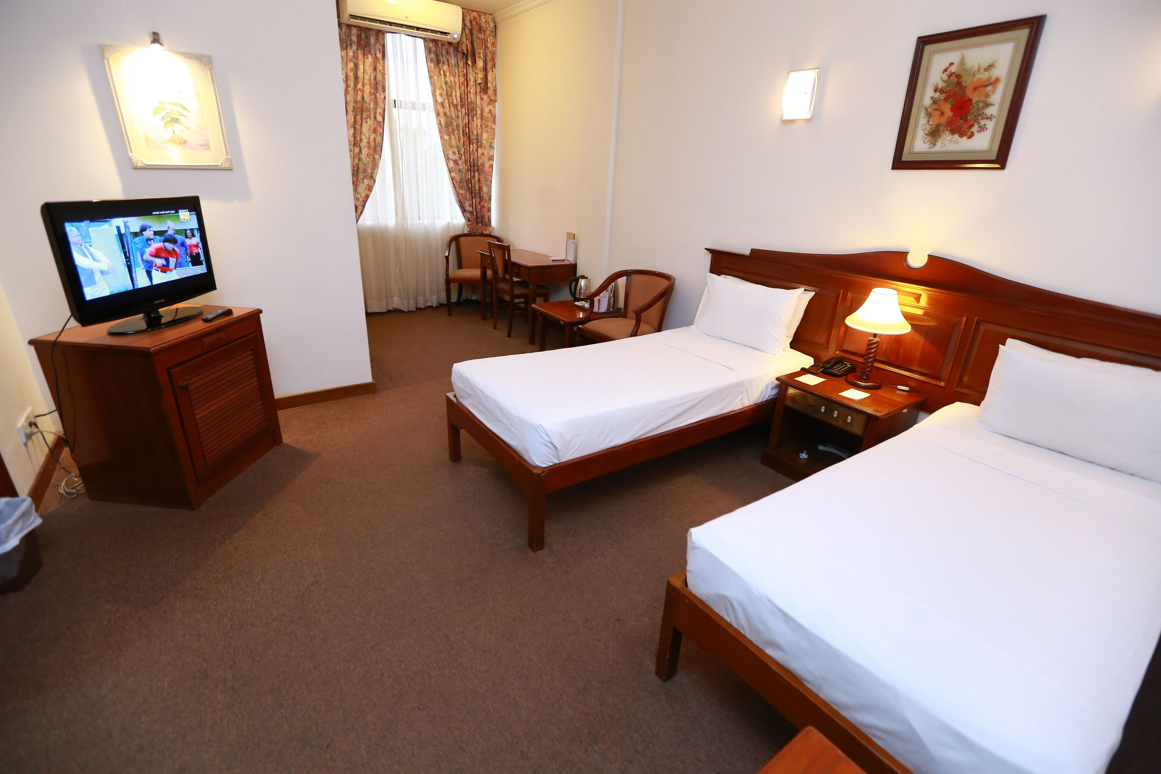 Habitación de hotel con dos camas, un escritorio, un televisor y una lámpara.