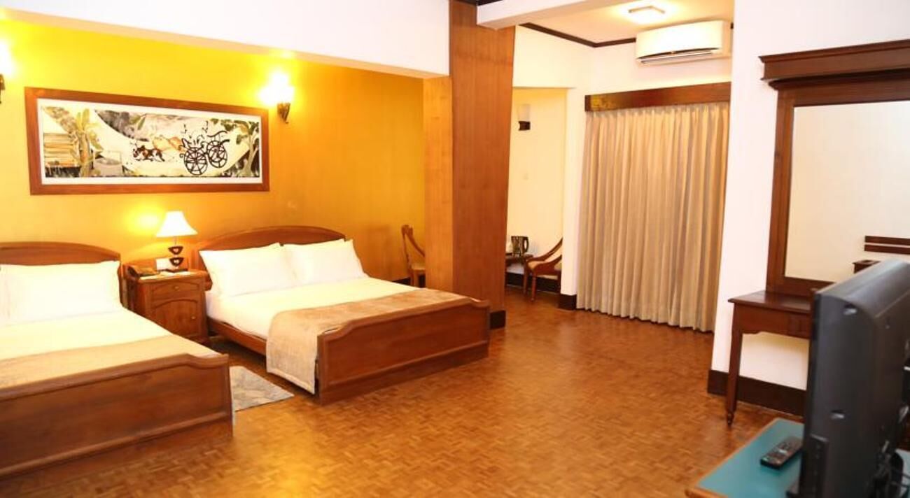 Une chambre d’hôtel avec deux lits, un bureau, une chaise, une télévision et un tableau au mur.