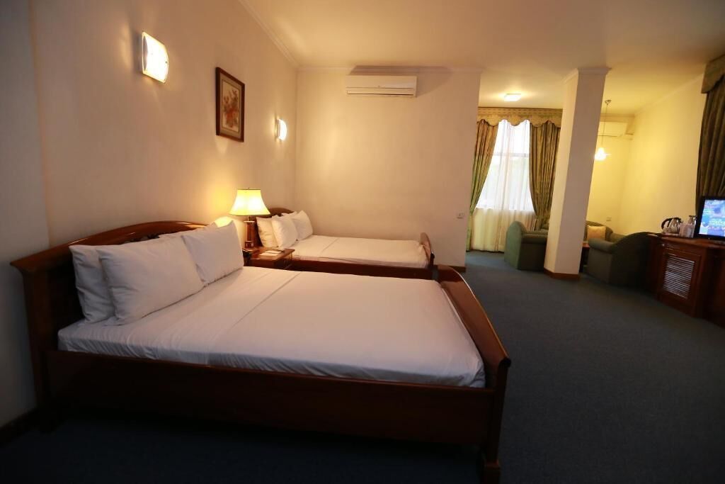 A hotel room with two beds, a desk with a lamp, a television, and a window with curtains.