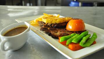 Ein Teller mit gegrilltem Steak, Pommes, einer gegrillten Tomate, grünen Bohnen und einer Tasse Kaffee auf einem Marmortisch.