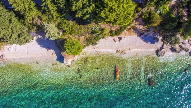 An aerial view of a beach with clear turquoise water, a sandy shore, and dense green foliage. - Hotel Labineca (Gradac)