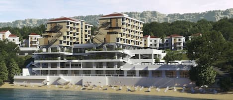 A coastal hotel with multiple buildings, a beach with sun loungers, and a mountainous backdrop.