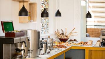 A breakfast bar with various food items, coffee machines, and hanging pendant lights.