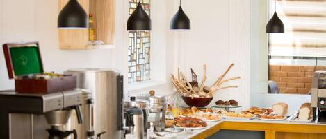 Una barra de desayuno con diversas opciones de comida, máquinas de café e iluminación colgante.
