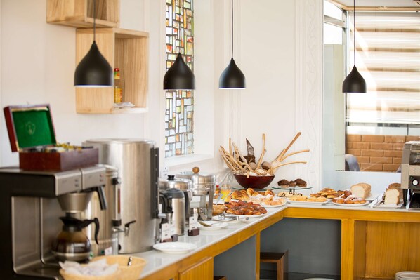A breakfast bar with various food items, coffee machines, and hanging pendant lights.