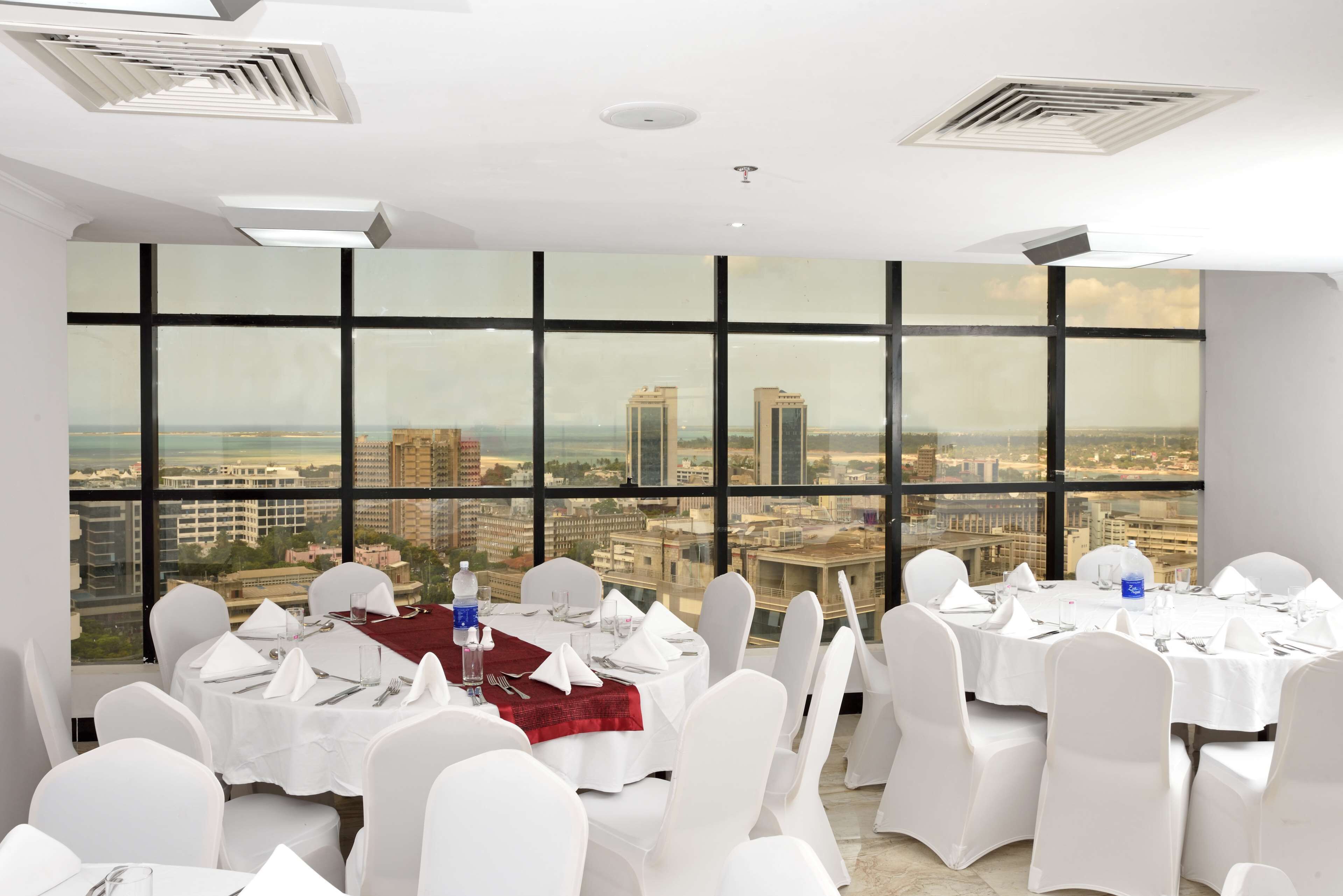 A conference room with tables set for a meeting, large windows with a city view, and white chairs.