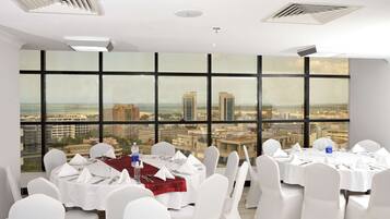 A conference room with tables set for a meeting, large windows with a city view, and white chairs.