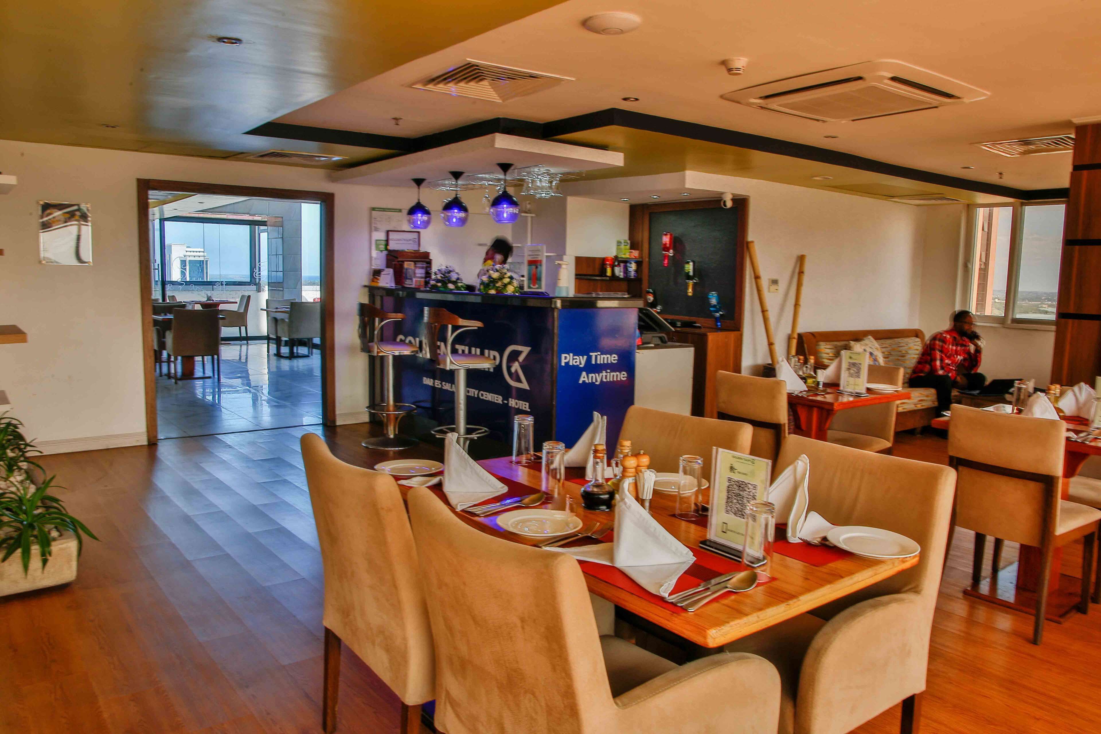 A hotel dining area with wooden tables, beige chairs, and a bar counter with a 'Play Time' sign.