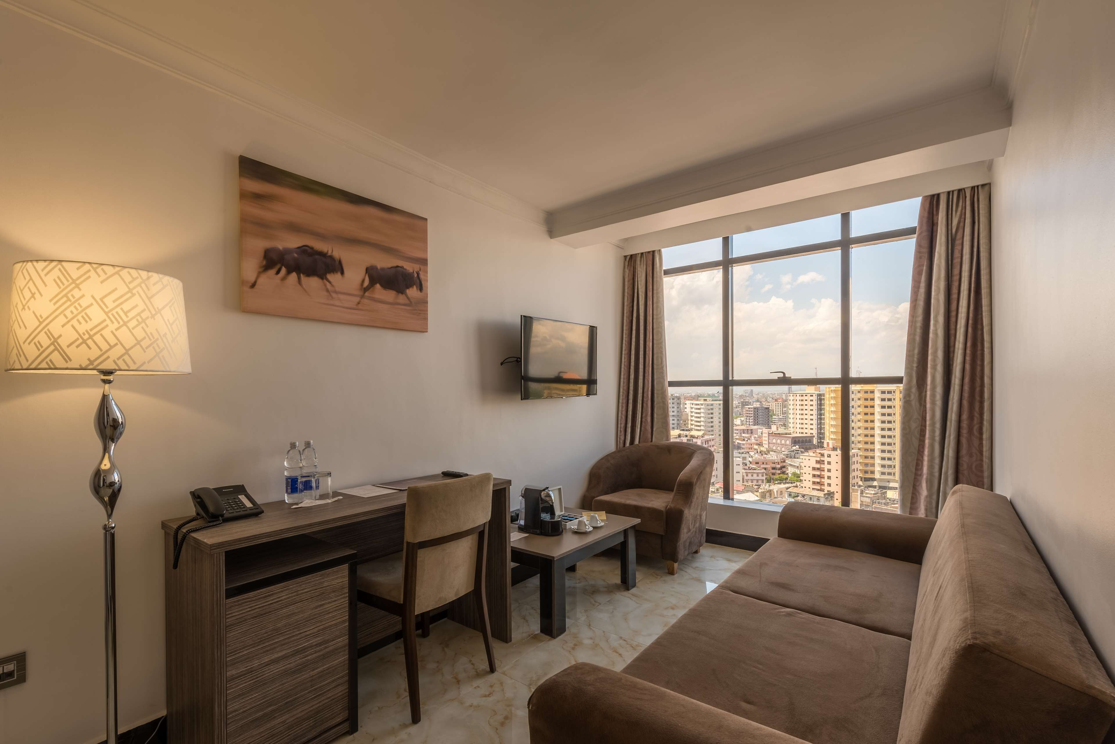 Habitació d'hotel amb escriptori, cadira, sofà i una finestra gran que ofereix vista a la ciutat.