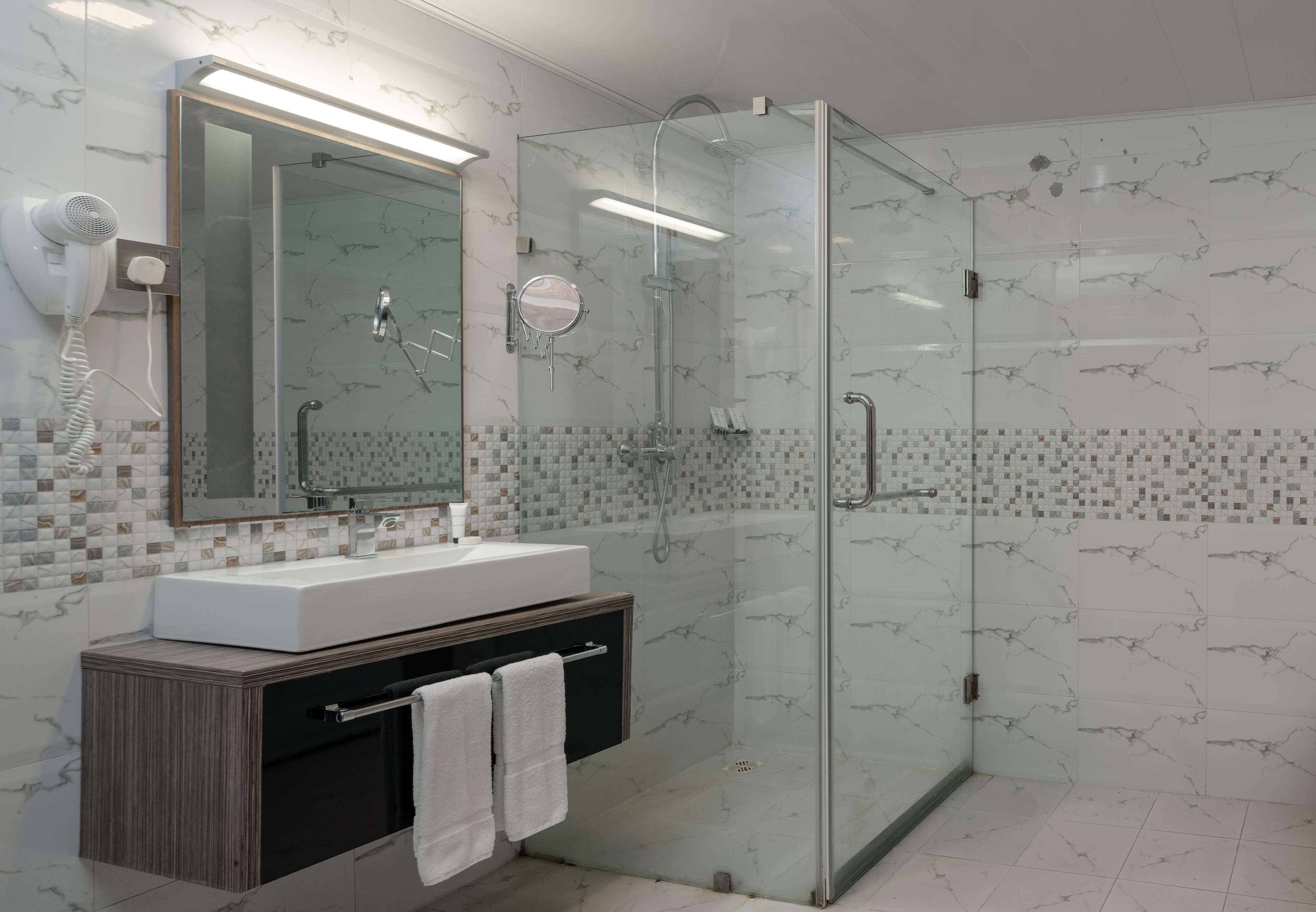A modern bathroom with a glass-enclosed shower, a white sink, and a vanity with a towel rack.