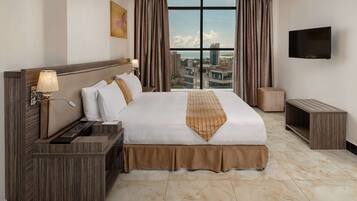 Hotelkamer met een groot bed, een televisie, een bureau en uitzicht op de stad door grote ramen.