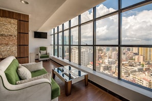 A modern living room with a large window, a sofa, a glass coffee table, and a city view.