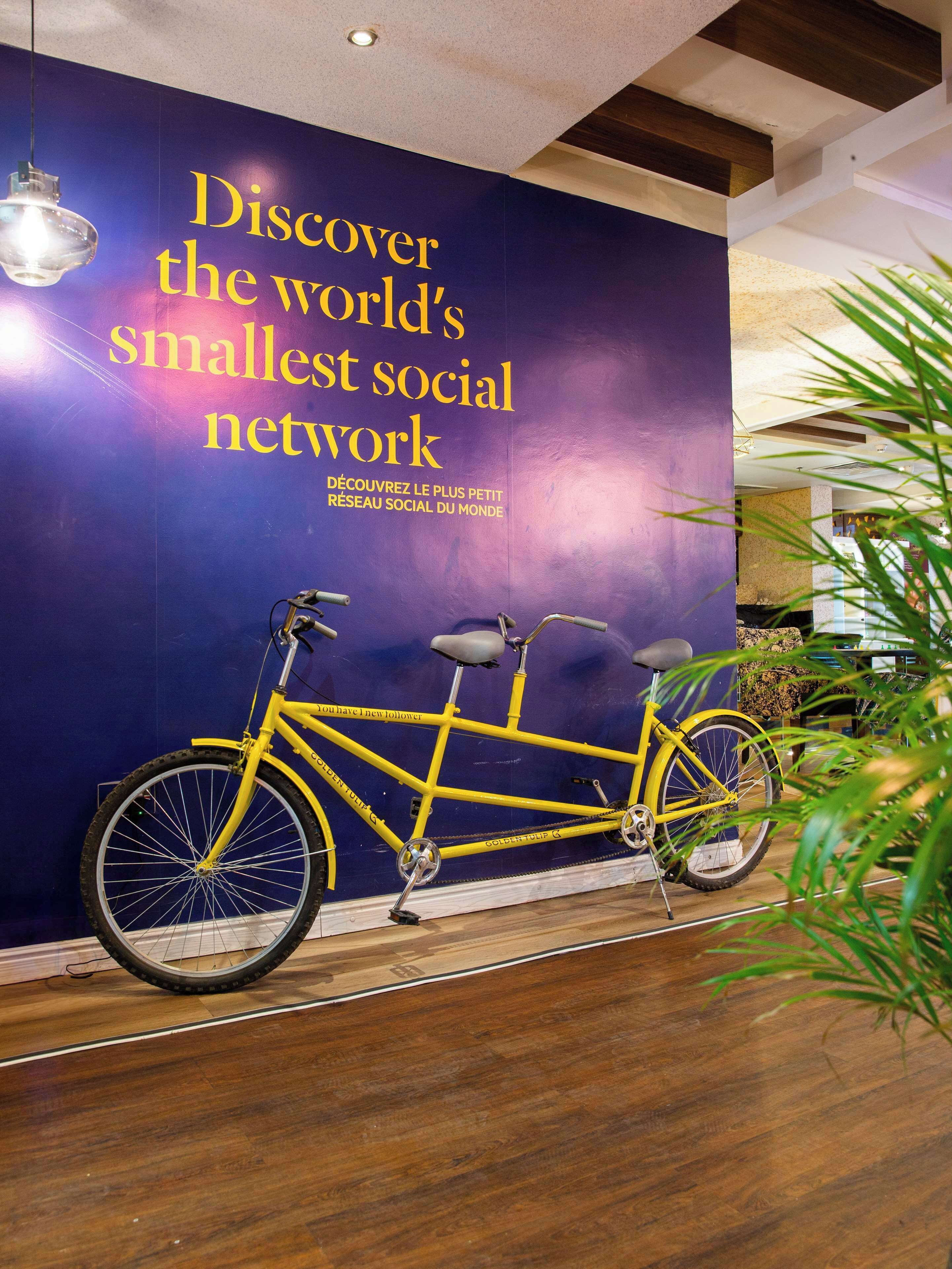 Una bicicleta amarilla frente a un muro con texto sobre descubrir la red social más pequeña del mundo.