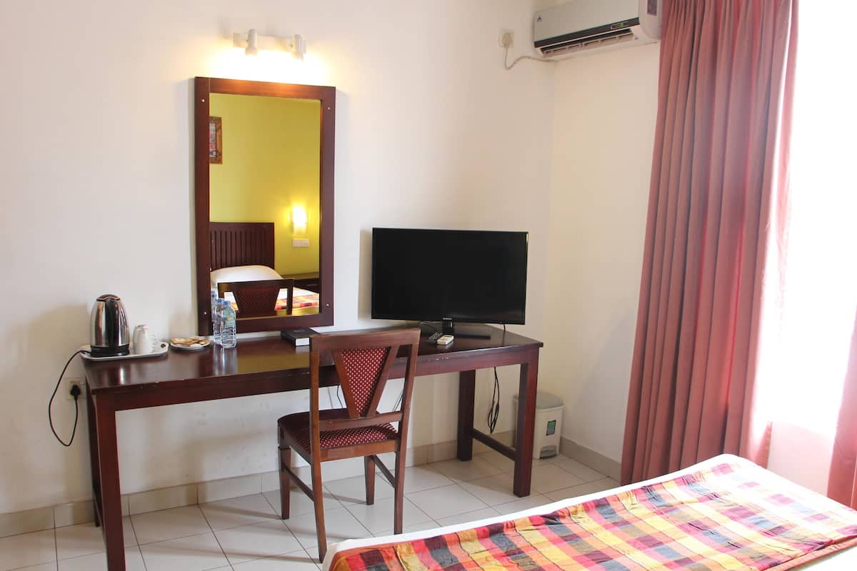 A hotel room with a bed, a desk with a chair, a television, a mirror, a kettle, and a water bottle.