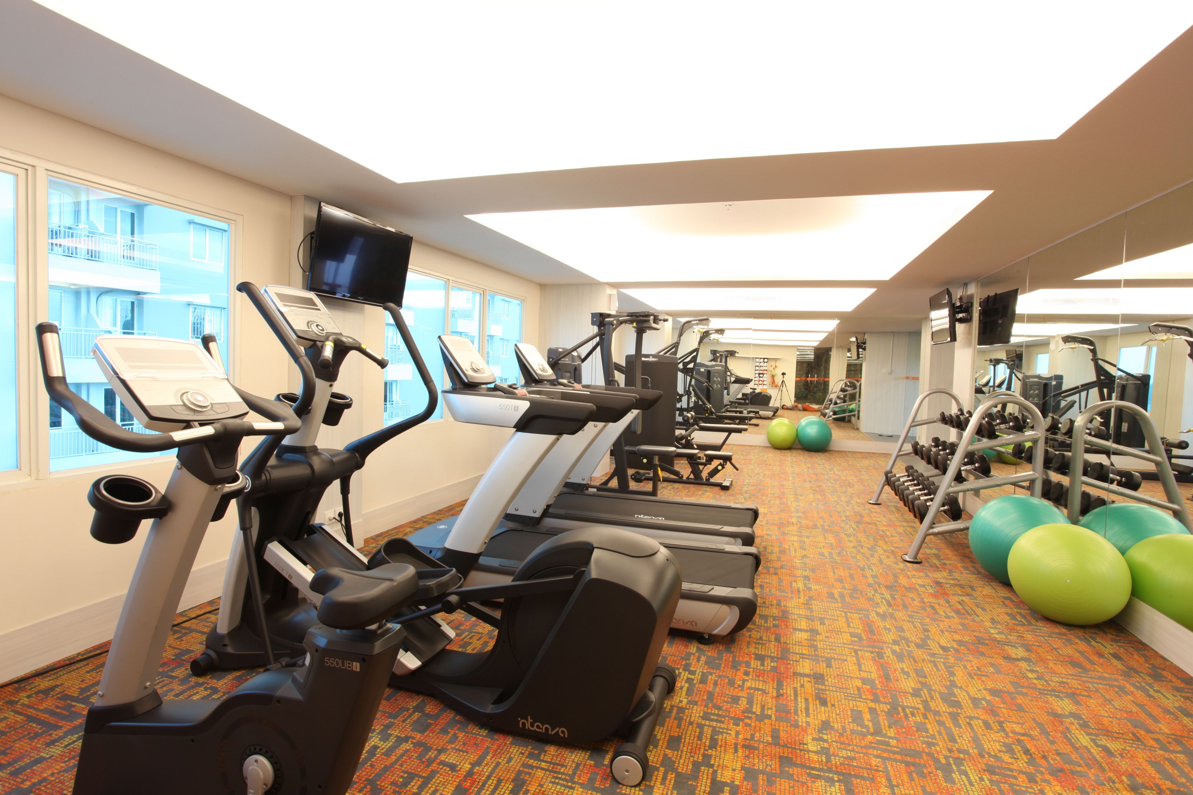 A gym with treadmills, elliptical machines, and exercise balls.