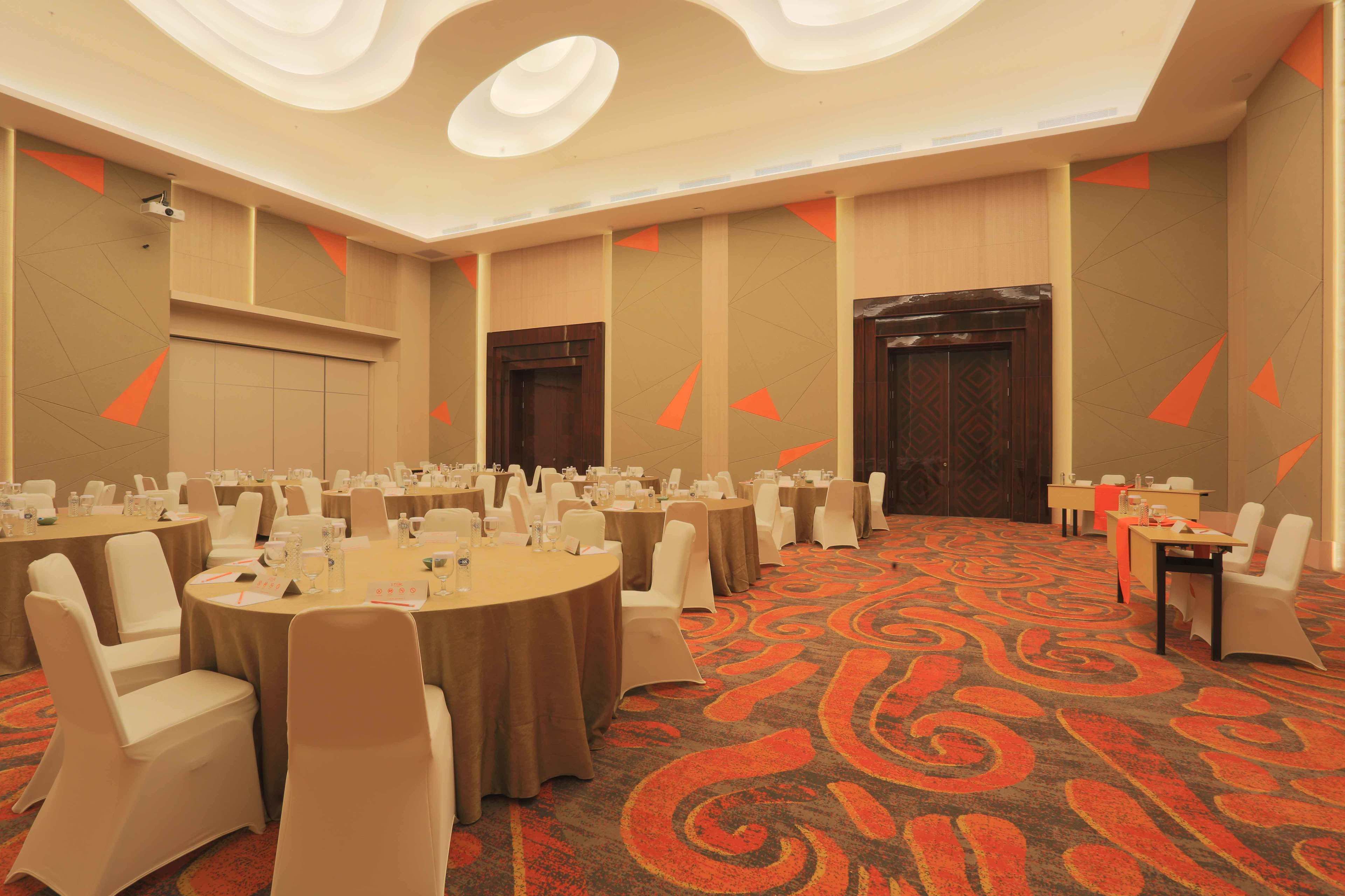 A conference room with round tables, white chairs, and a patterned carpet.