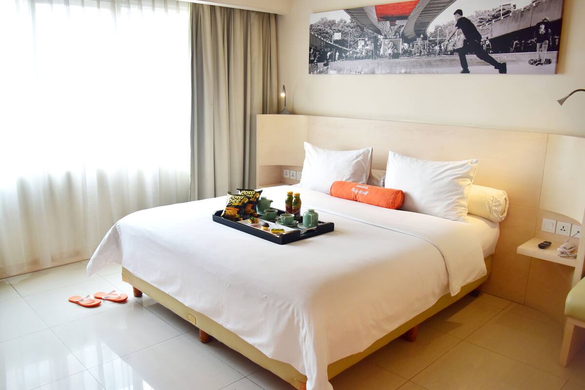 A hotel room with a neatly made bed, a tray with breakfast items, and a painting on the wall.