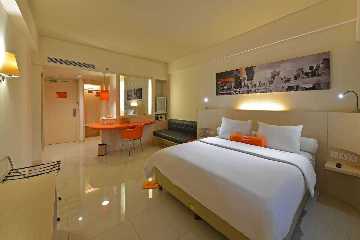 A hotel room with a large bed, a desk with a chair, a small table, and a large mirror.