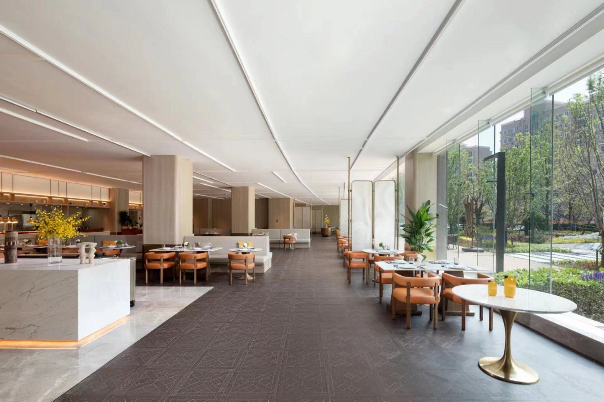 A spacious hotel lobby with a central reception area, multiple dining tables, and large windows offering a view of the outdoors.