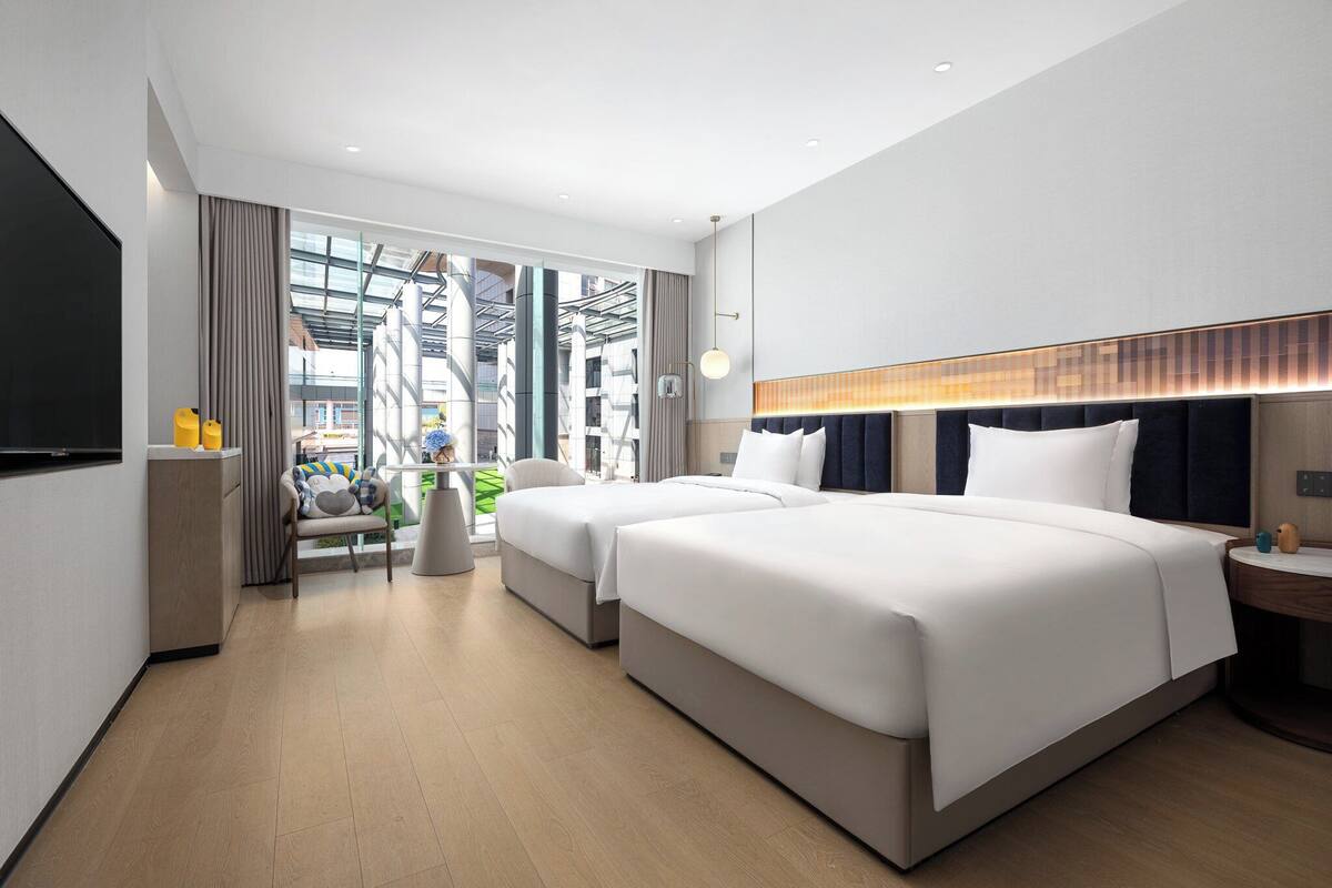 Ein modernes Hotelzimmer mit zwei Betten, einem Schreibtisch und Blick auf die Stadt.