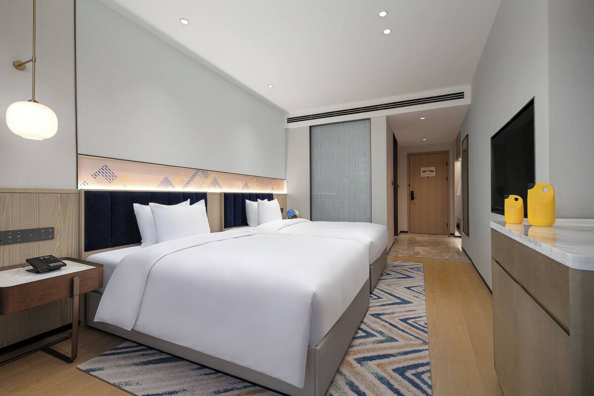 Ein modernes Hotelzimmer mit einem großen Bett, Nachttischen, einem Schreibtisch, einem Flachbildfernseher und einem gemusterten Teppich.