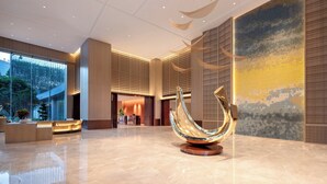 A spacious lobby with a modern reception desk, a large decorative sculpture, and a view of the outdoors through large windows. - voco Lianyungang Haizhou Bay by IHG (Lianyungang)