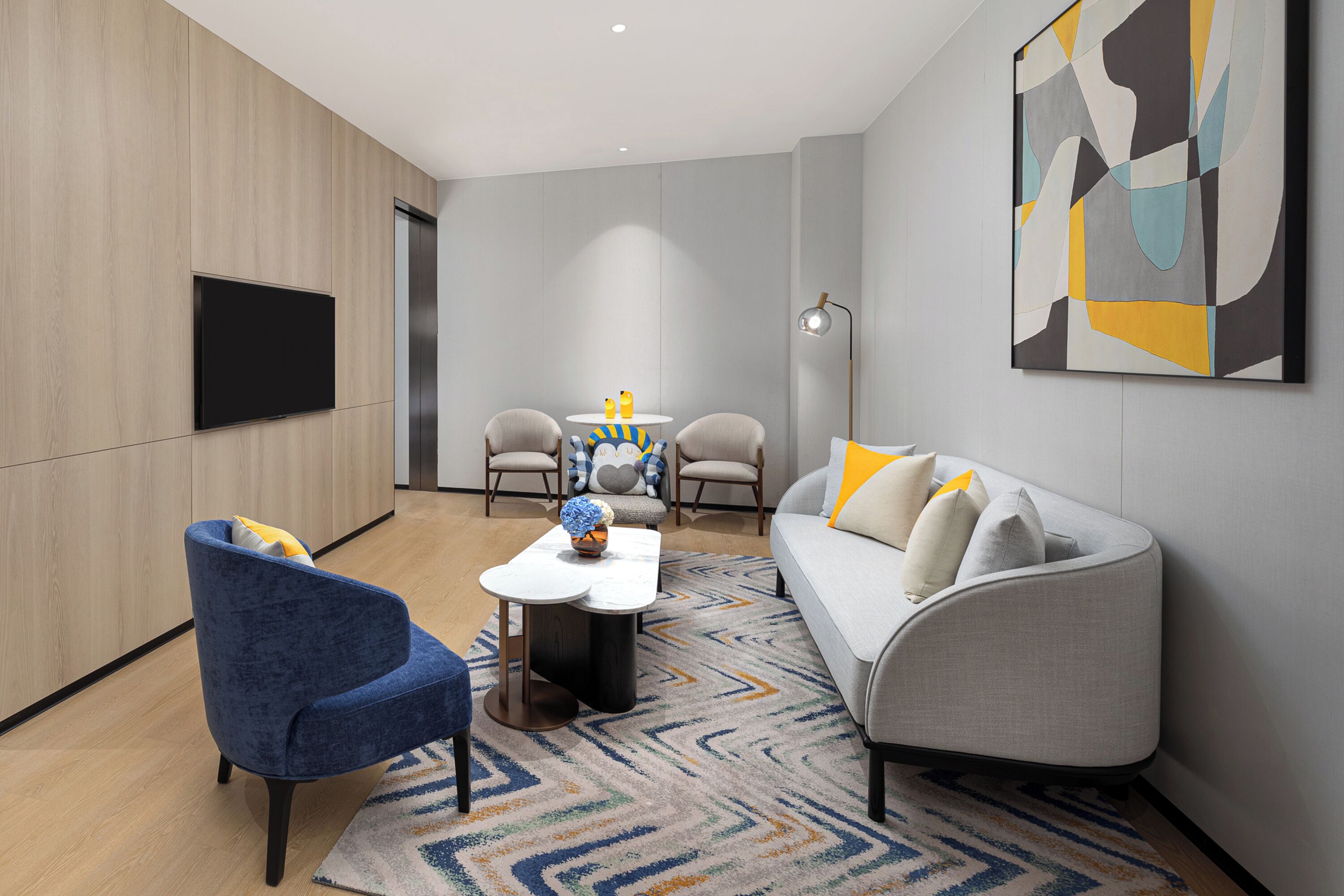 Un salon moderne comprenant un canapé, un fauteuil, une table basse et un téléviseur à écran plat fixé au mur.