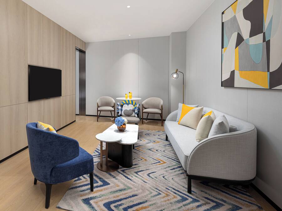 Un salon moderne comprenant un canapé, un fauteuil, une table basse et un téléviseur à écran plat fixé au mur.