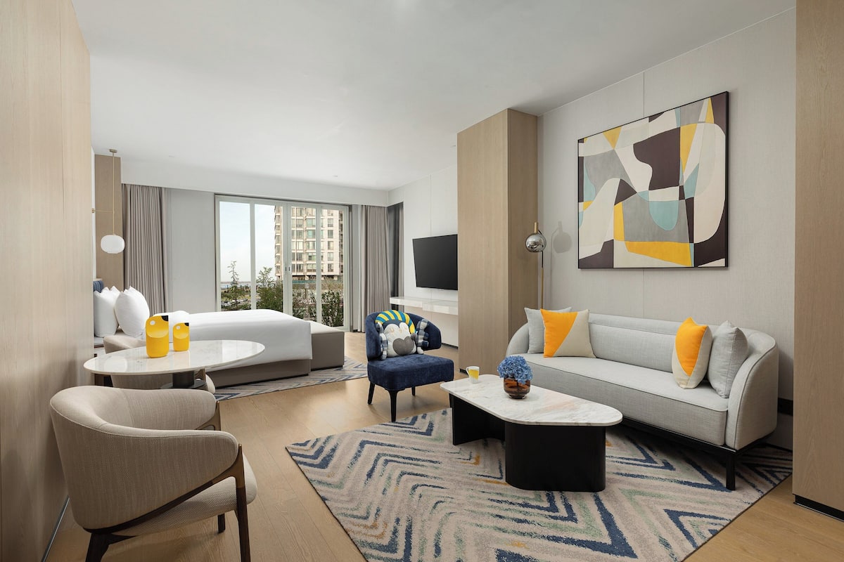 Ein modernes Hotelzimmer mit einer Couch, einem Sessel, einem Couchtisch und einem großen abstrakten Gemälde an der Wand.