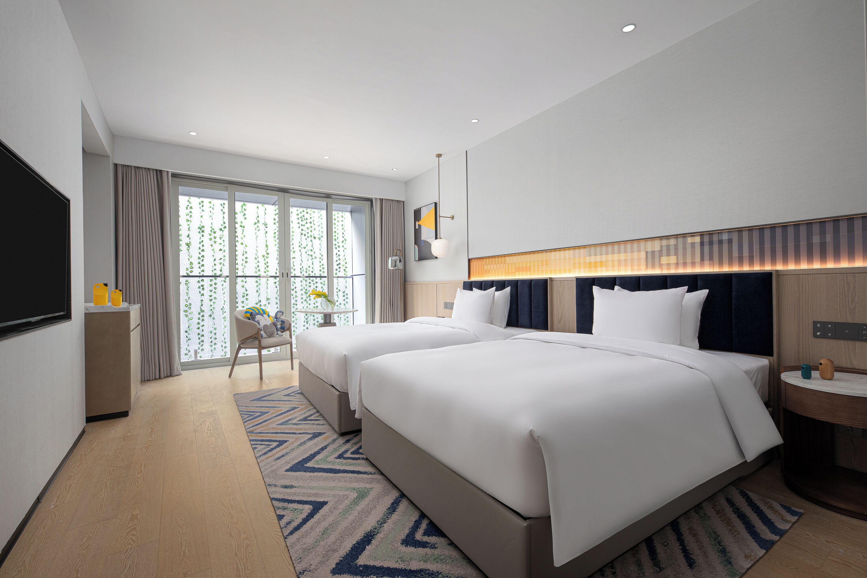 A modern hotel room with two beds, a desk, and a large window with curtains.