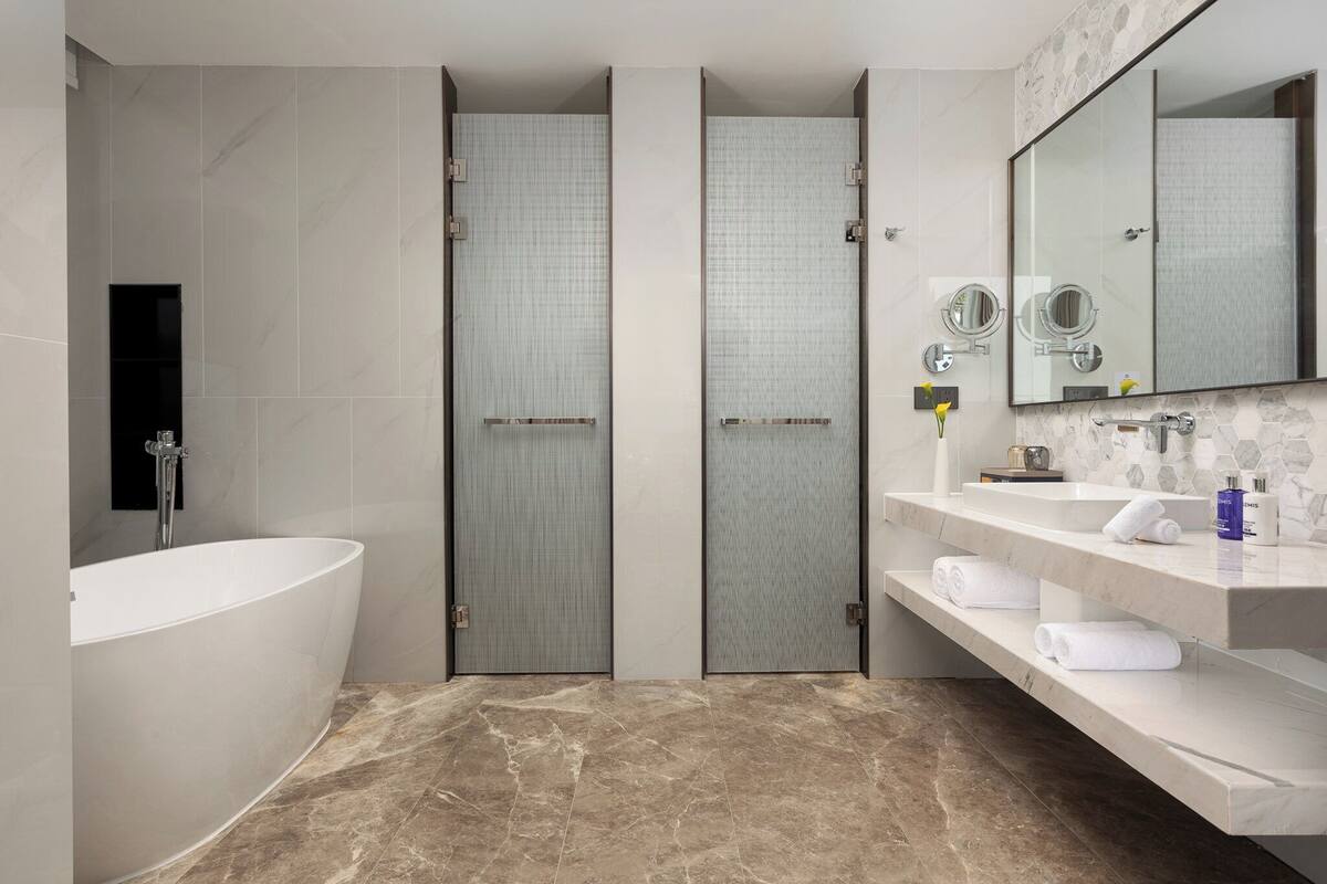 Une salle de bain moderne avec une baignoire sur pieds, un meuble-lavabo doté d’un grand miroir et un espace douche avec des portes en verre dépoli.
